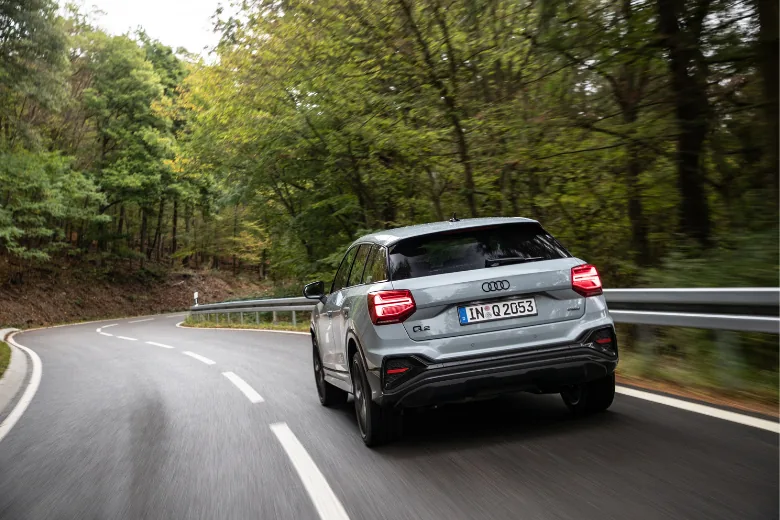 Audi Q2 gris en conducción por una carretera entre árboles
